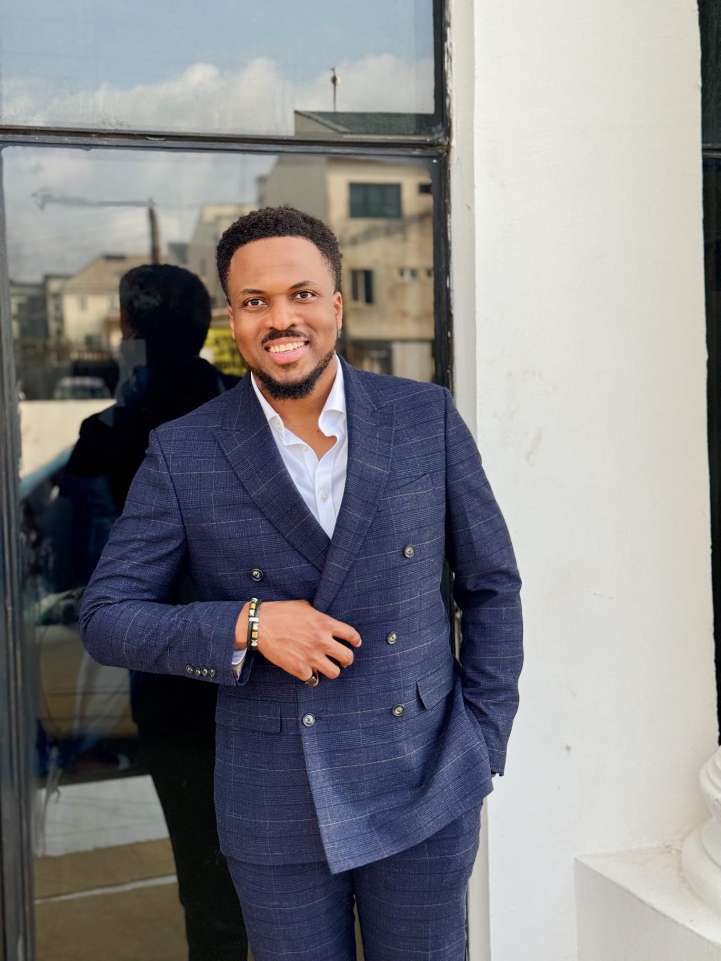 Uche Ojukwu in a checked double-breasted suit, leaning against an office doorway.
